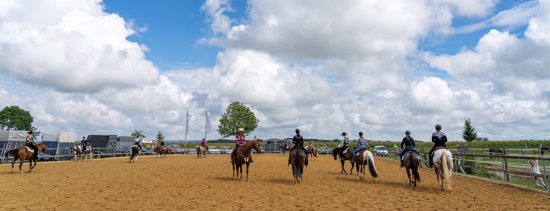 Reiter auf dem Außenreitplatz der Reitsportanlage Haldau, im Hintergrund Pferdeanhänger und Fahnen