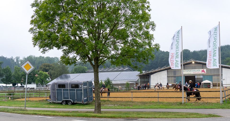 Die Reitsportanlage Haldau mit Werbefahnen und Reitplatz, Reiter vor der Halle
